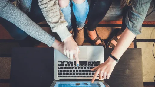 Three people sitting on a couch pointing at a laptop.